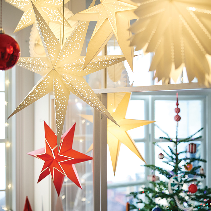 Lámparas de papel en forma de estrellas luminosas colgadas cerca del árbol navideño.