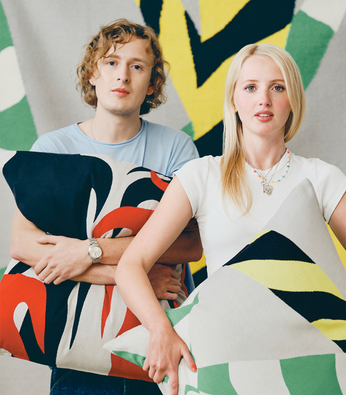 Couple posing while holding decorative cushions with colorful geometric patterns.