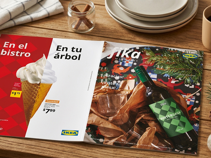 Front cover of IKEA's "Fika Magazine" placed on a terracotta table next to a plate of food, a knife, a fork, and a glass of pink beverage.