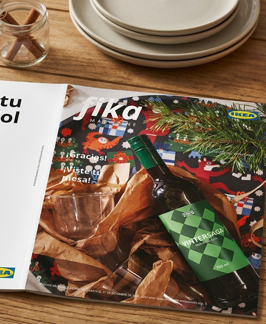 Front cover of IKEA's "Fika Magazine" featuring a top-down view of a table spread with snacks like potato chips, chocolate squares, nuts, and candies.